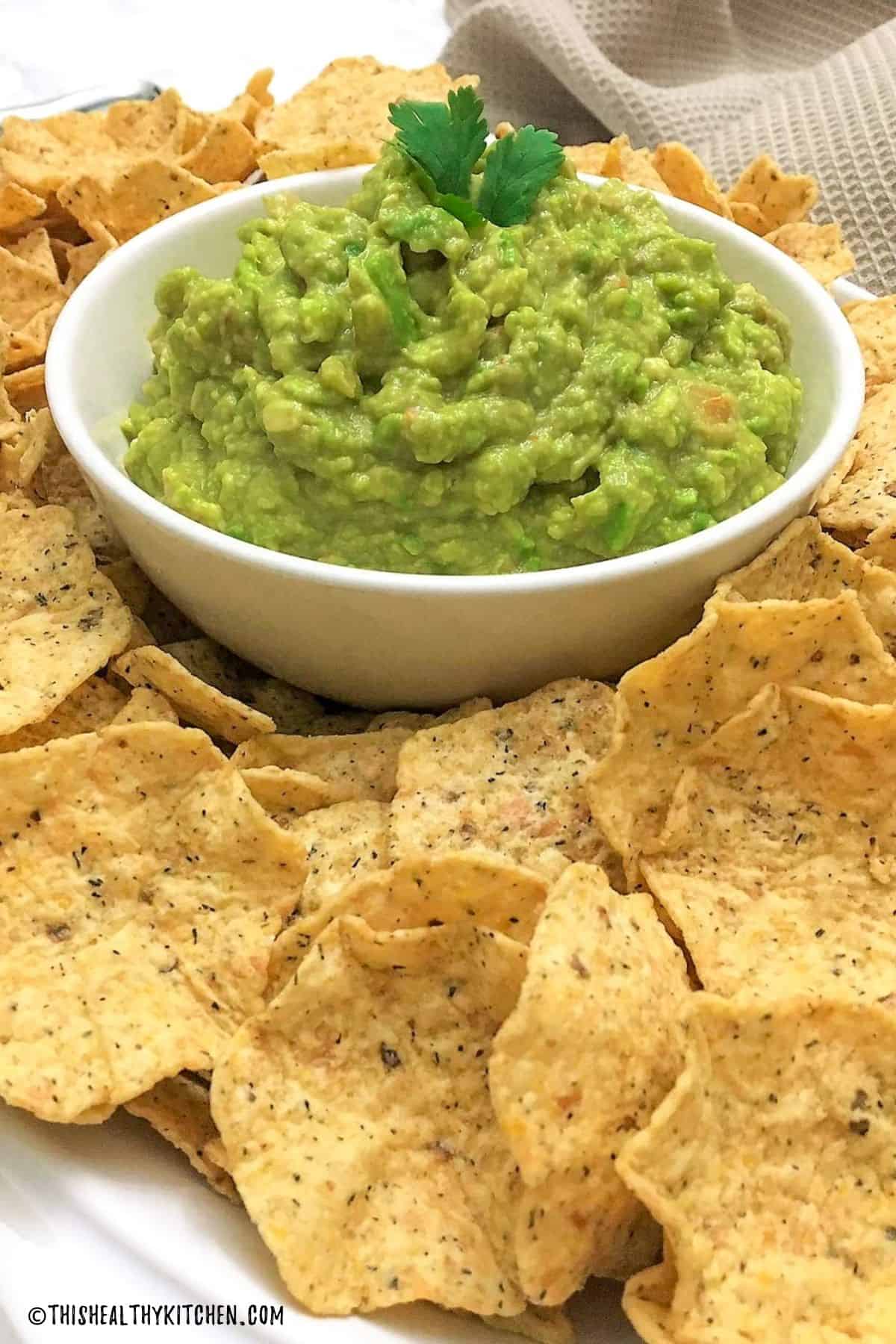 Bowl of guacamole with tortilla chips all around it.