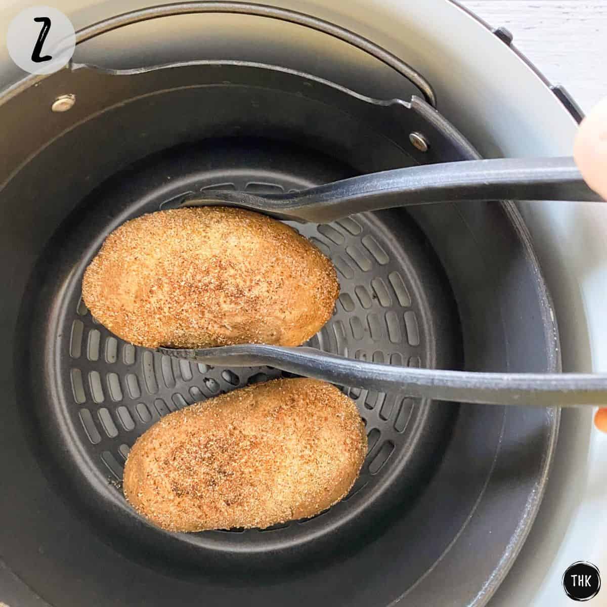 Tongs flipping russet potatoes inside air frying basket.