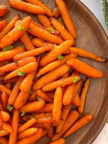 Baby carrots in brown bamboo plate with parsley garnish.