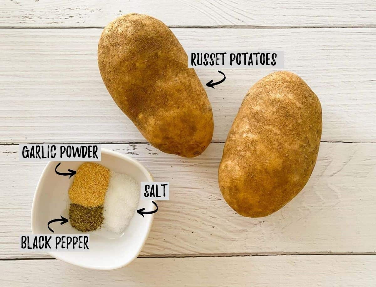 Russet potatoes and a bowl of seasoning on white deck.