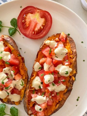 Baked sweet potatoes in white plate with sour cream, tomato and parsley on top.