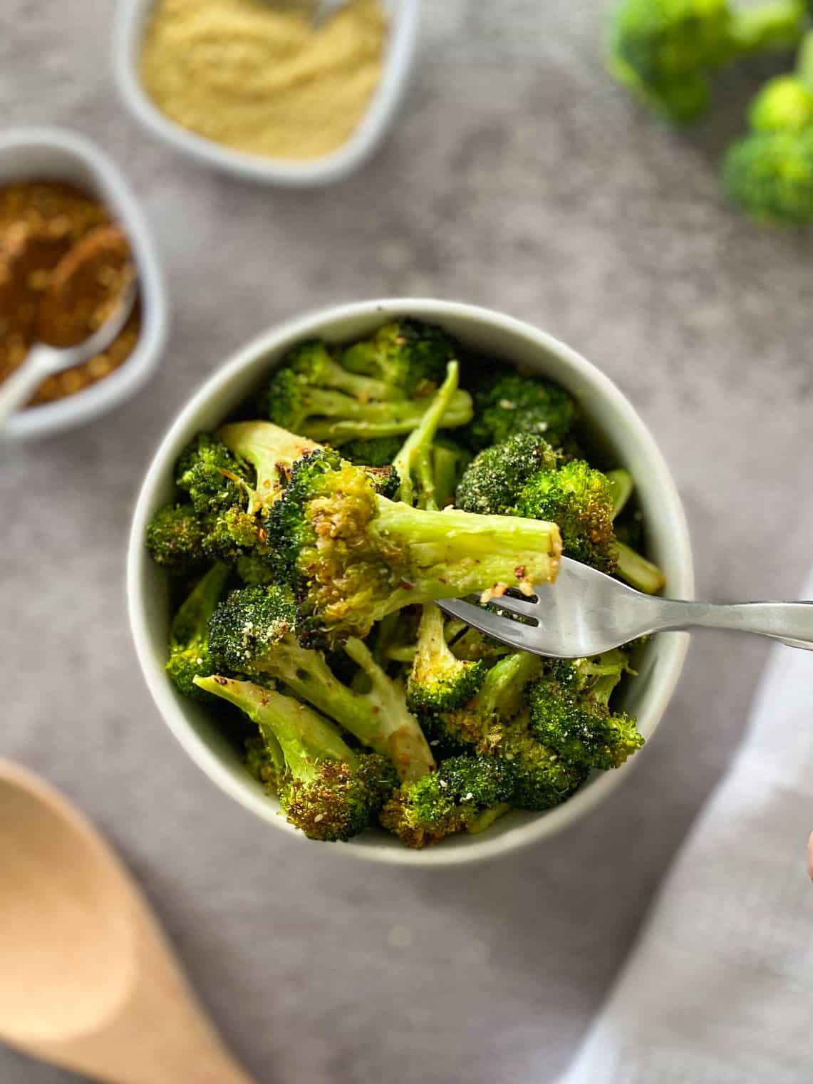 Fork holding up a broccoli floret over a bowl of more broccoli.
