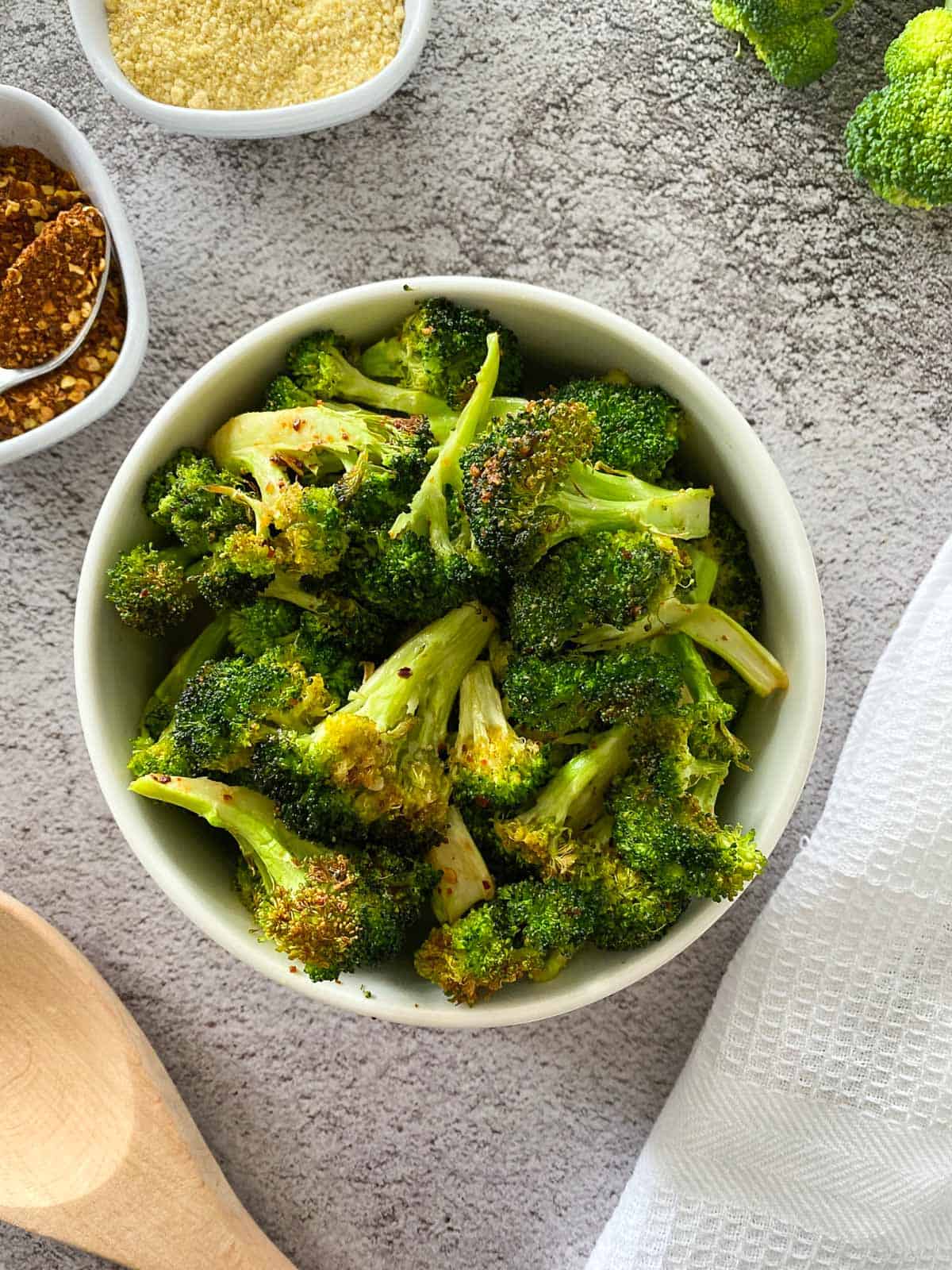 Air fried broccoli in white bowl with white dish towel beside it.