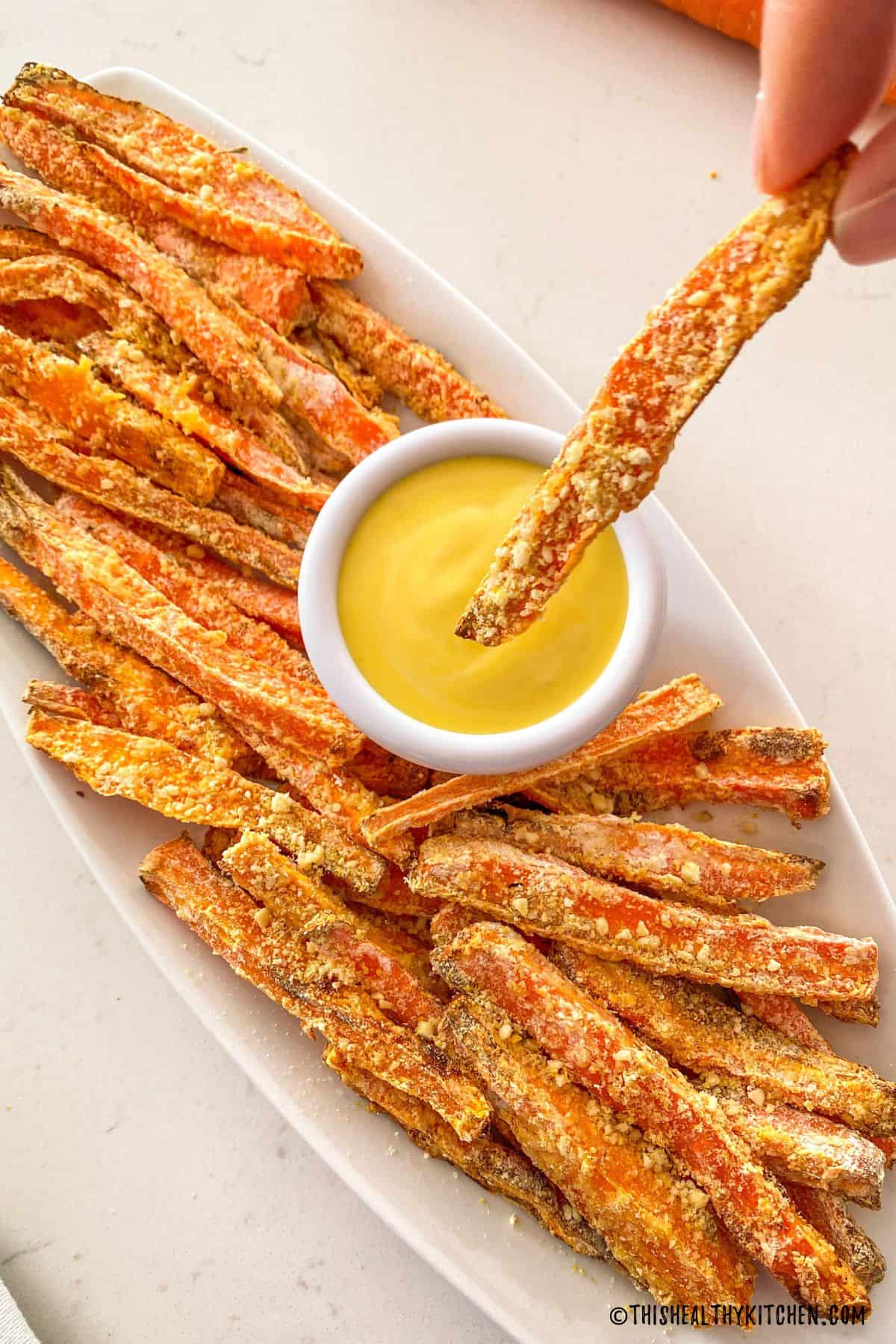 Carrot fry being dipped into yellow sauce.