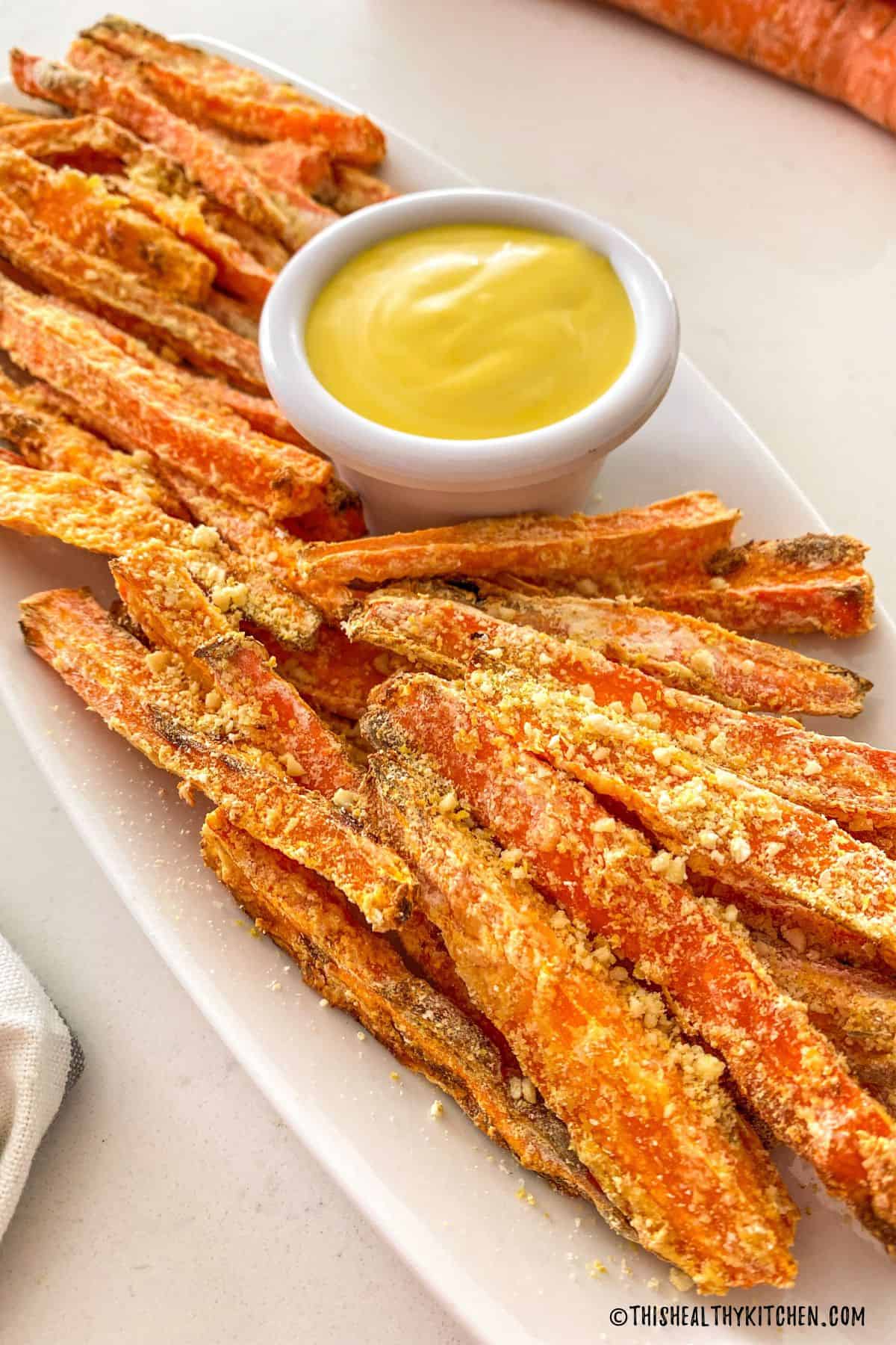 Carrot fries on white serving dish with small dipping bowl with yellow sauce.