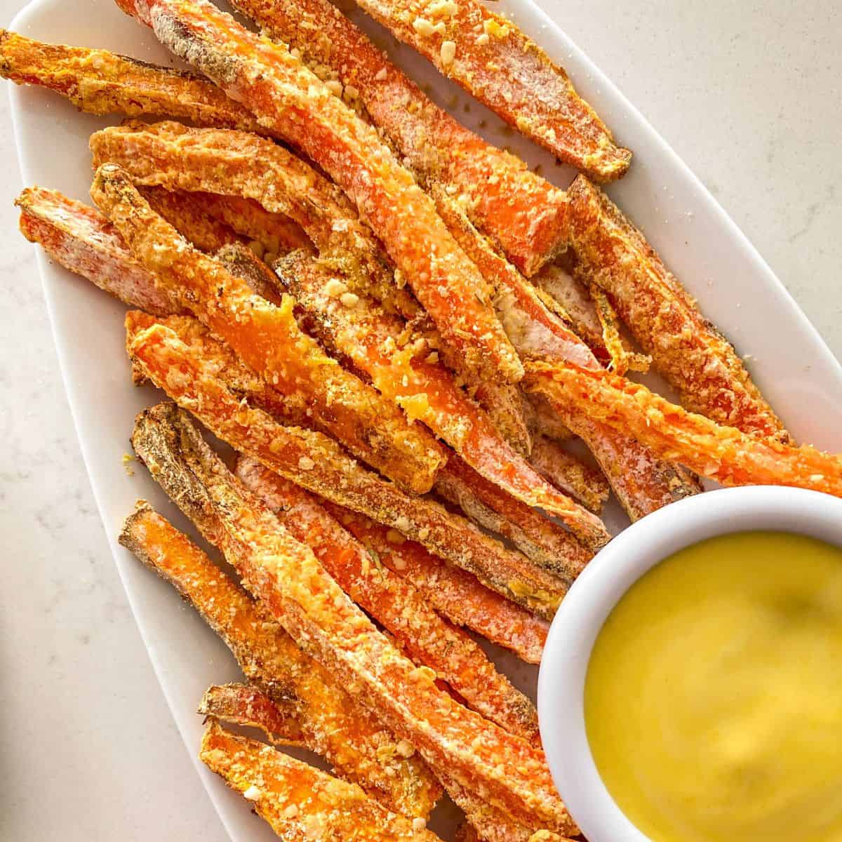 Carrot fries on white platter with yellow dipping sauce.