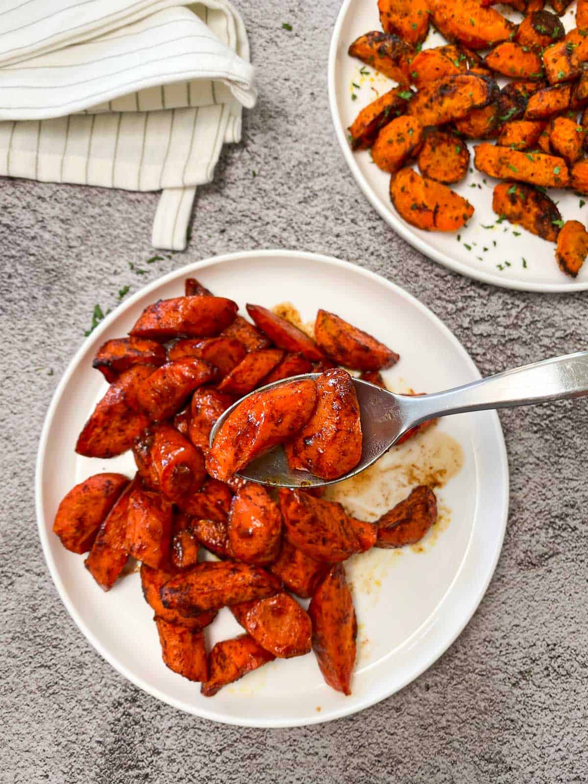 air fryer sweet carrots in white serving dish with spoon holding up two pieces of the carrots