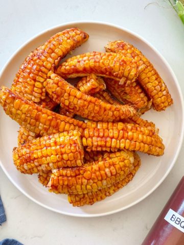 Air fried corn ribs with bbq sauce on top in white plate.