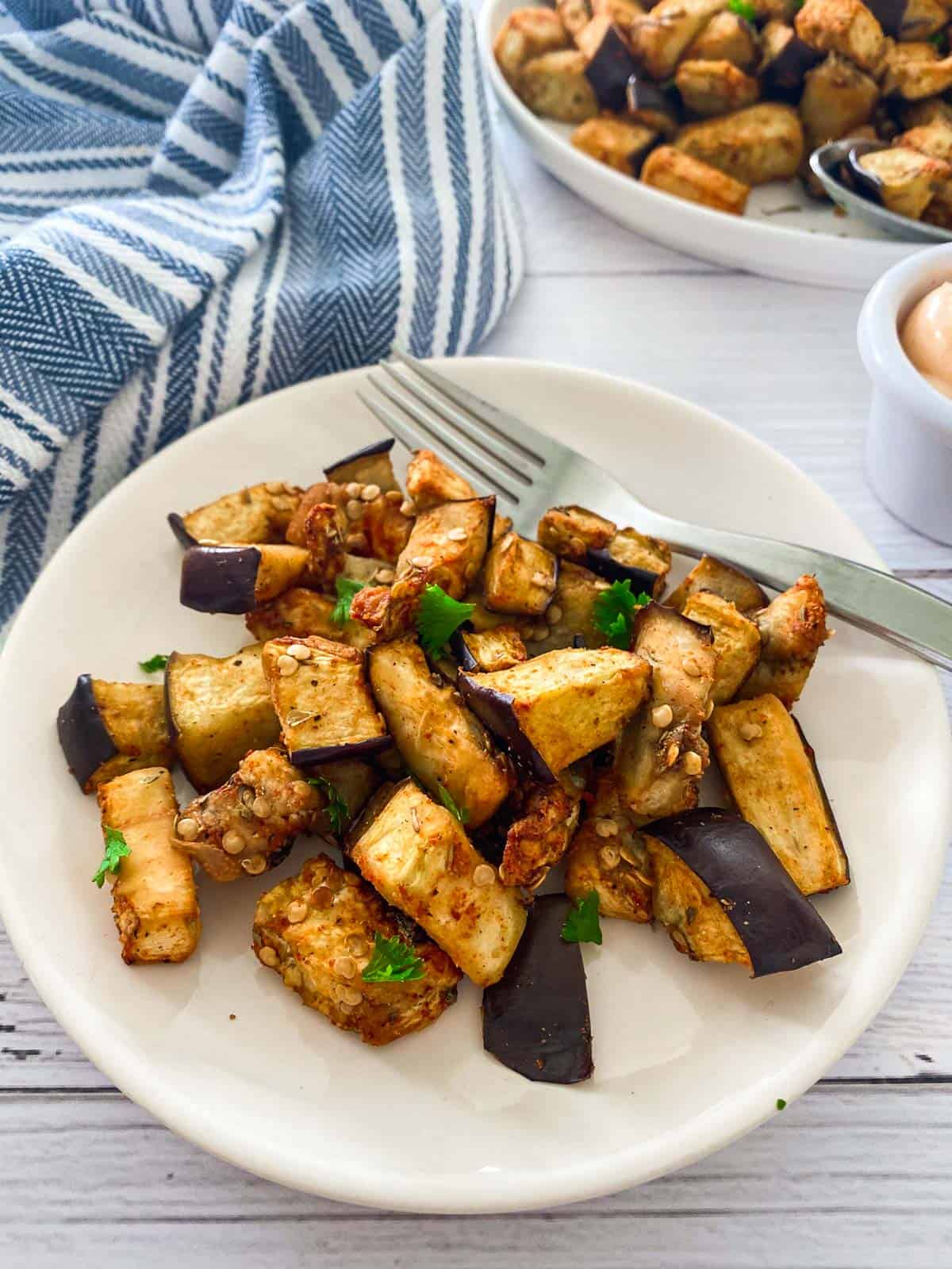 White plate with cooked eggplant pieces inside, sprinkled with parsley.
