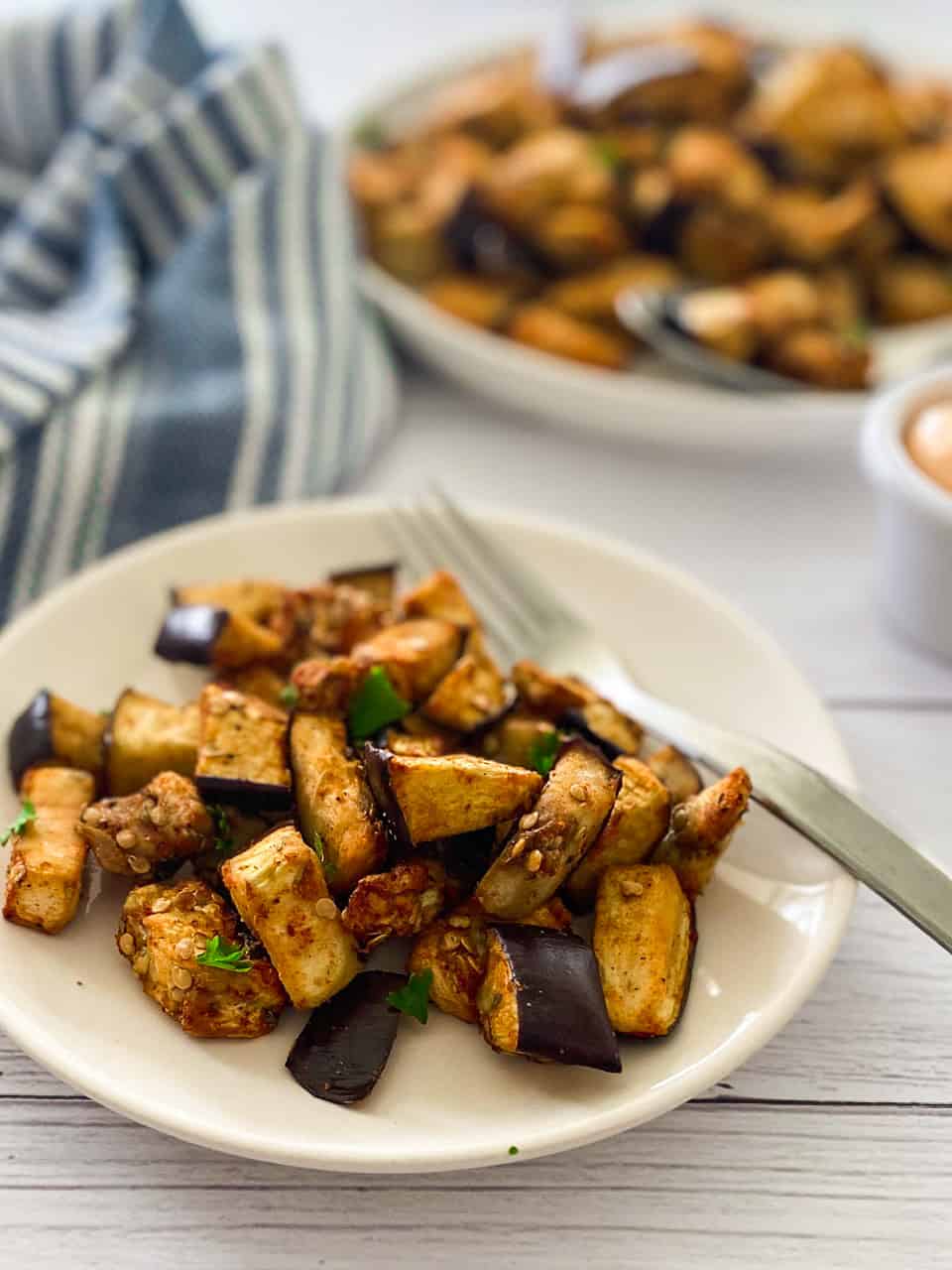 Plate of air fried eggplant with fork inside and platter in the background.