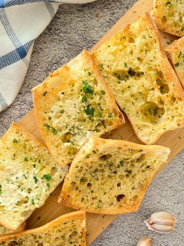 Slices of garlic bread on wooden cutting board.