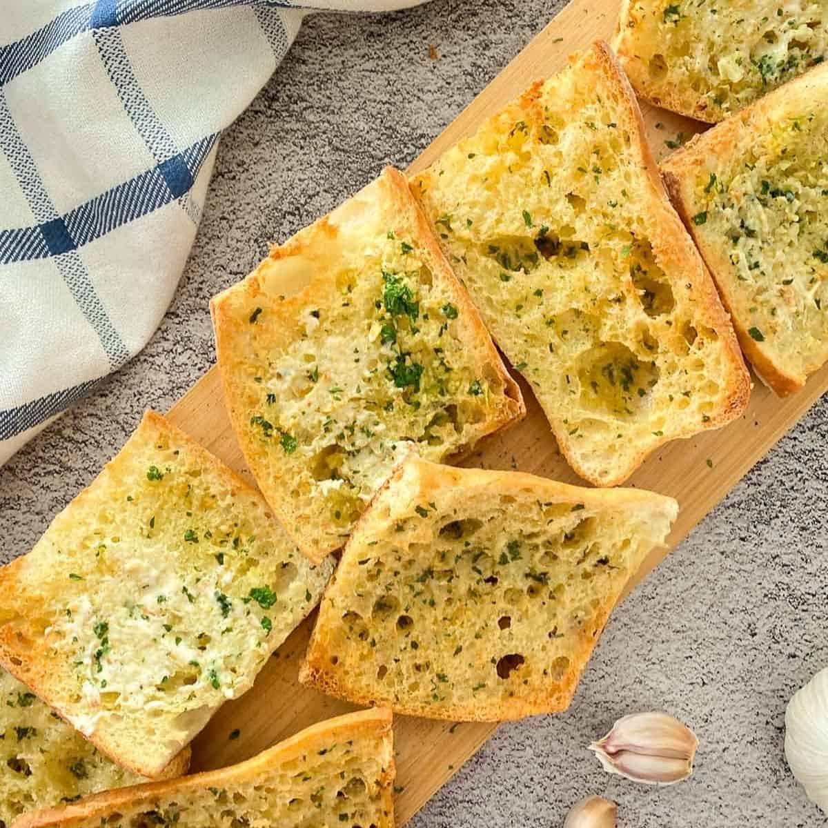 Slices of garlic bread on wooden cutting board.