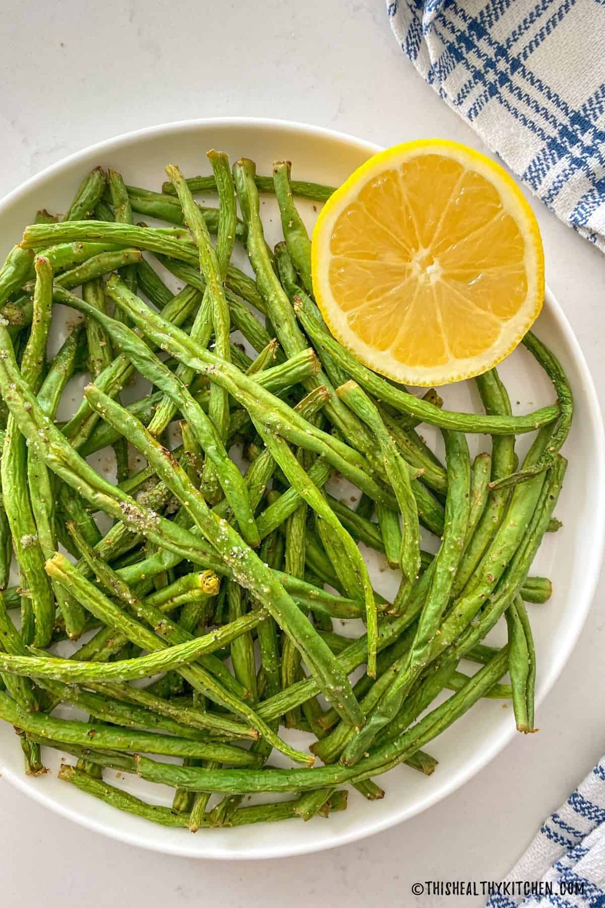 Green beans in white plate with halved lemon on the side.