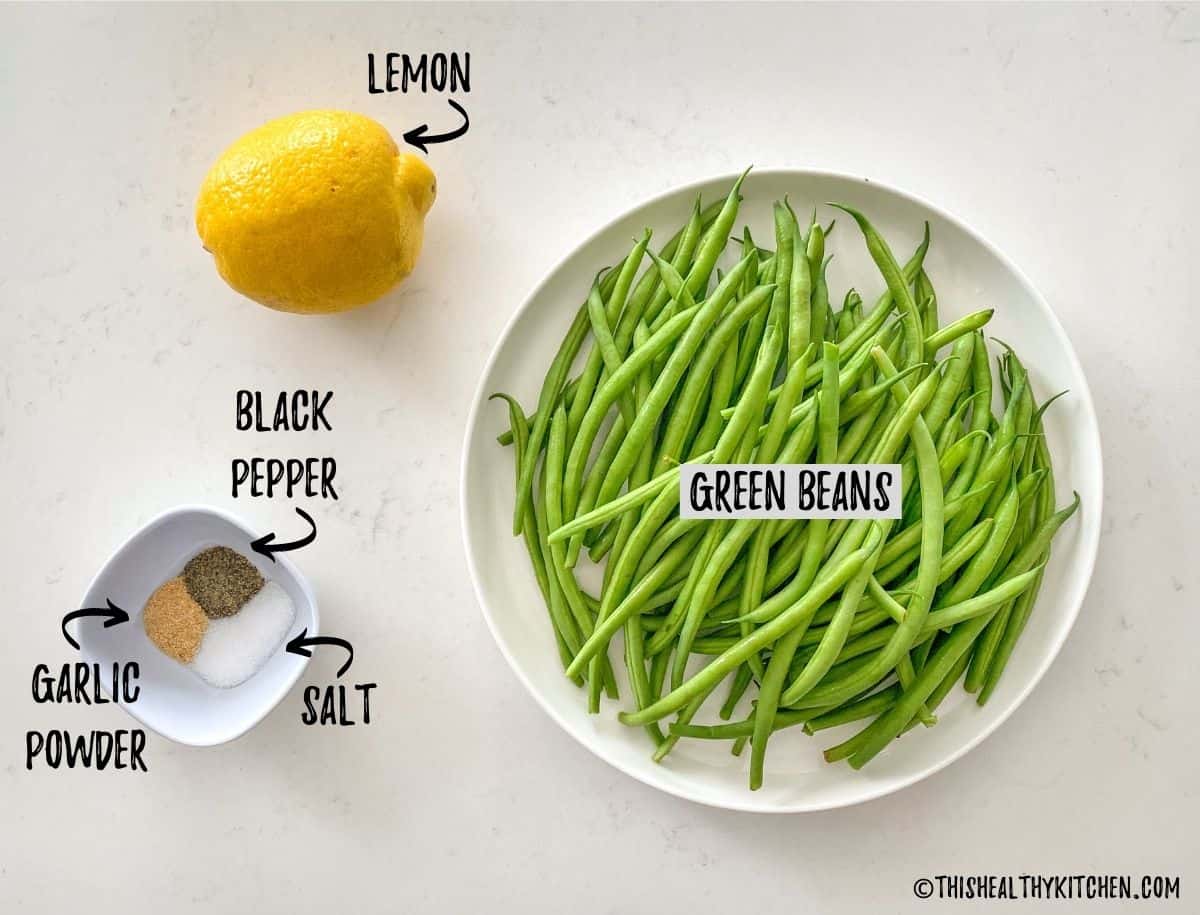 Plate of green beans, lemon and spices scattered on kitchen counter.