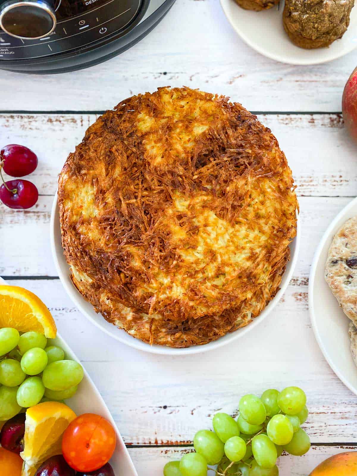 large round hash browns in plate with air fryer in the background and fruit scattered around
