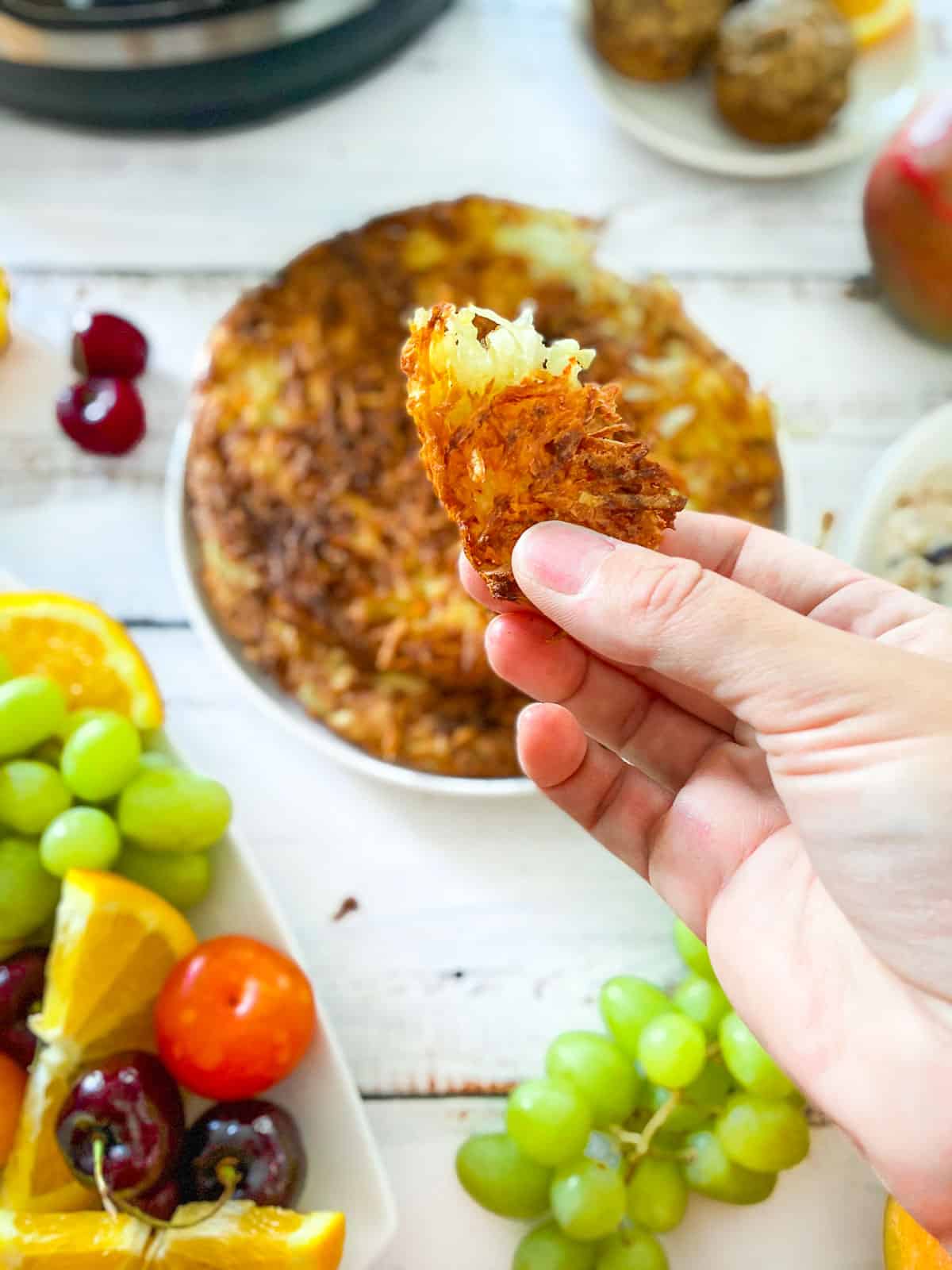 piece of hash brown being held up with hand above the plate of hash browns below