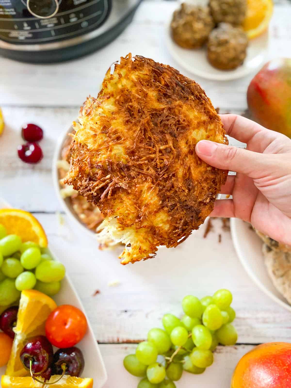 hand holding up hash brown wedge with air fryer and fruit in the background