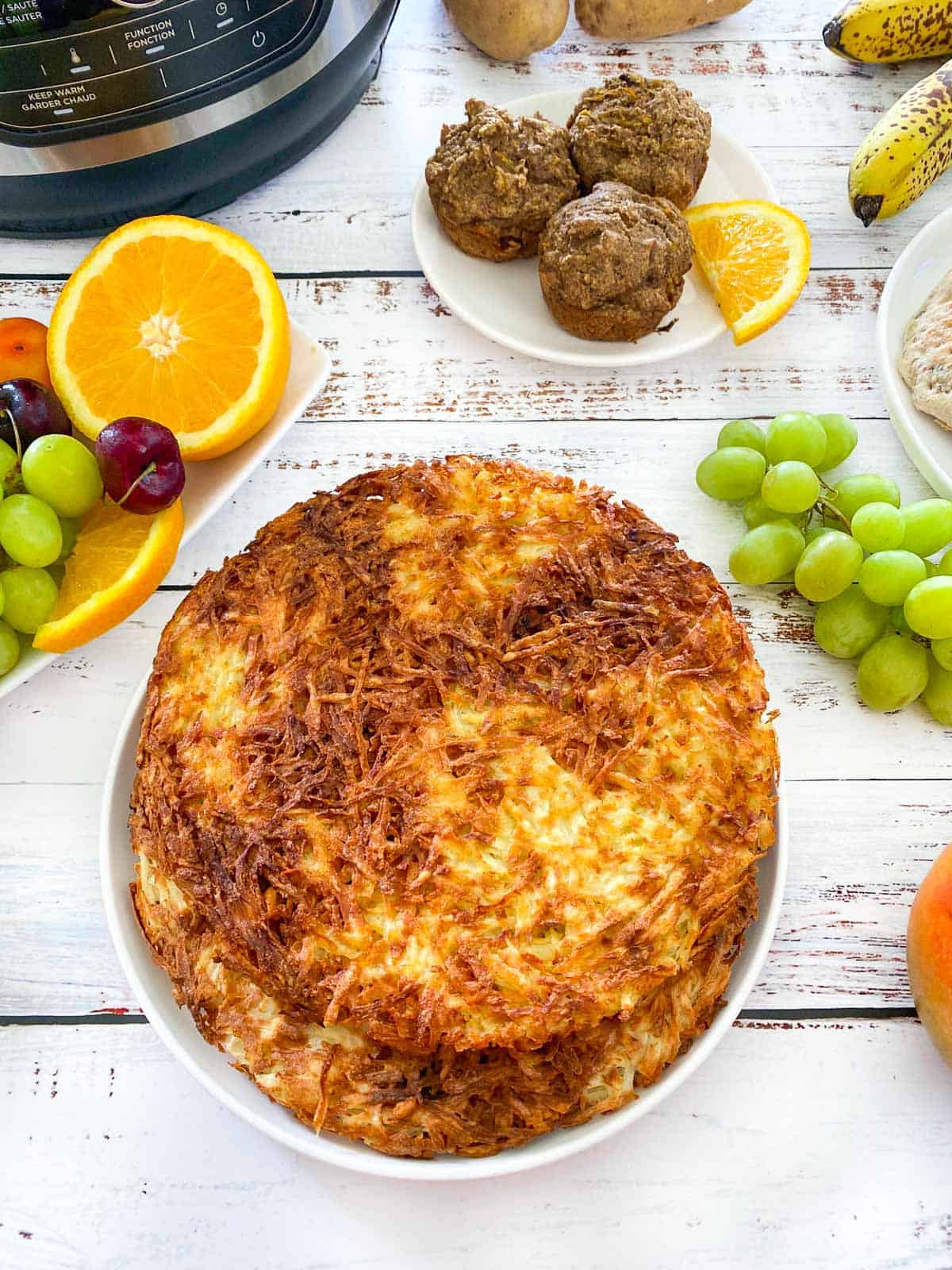 plate of hash browns with tray of fruit beside it and plate of muffins above