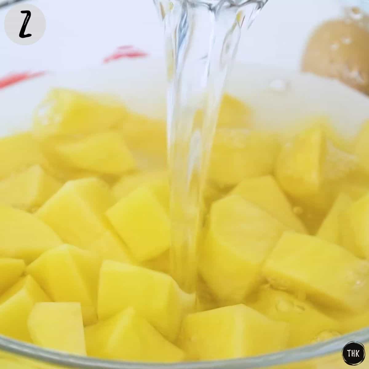 Water being poured into bowl of chopped potatoes.