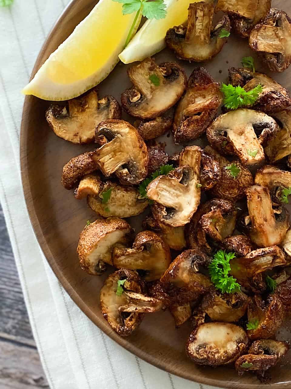 air fried mushrooms on brown plate with lemon wedges on the side.