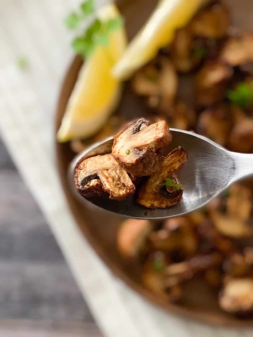 Spoon holding up cooked mushrooms with dish of more mushrooms below.