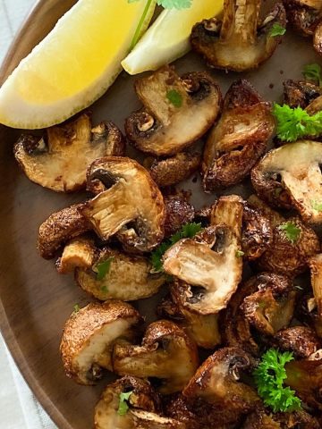air fried mushrooms on brown plate with lemon wedges on the side.