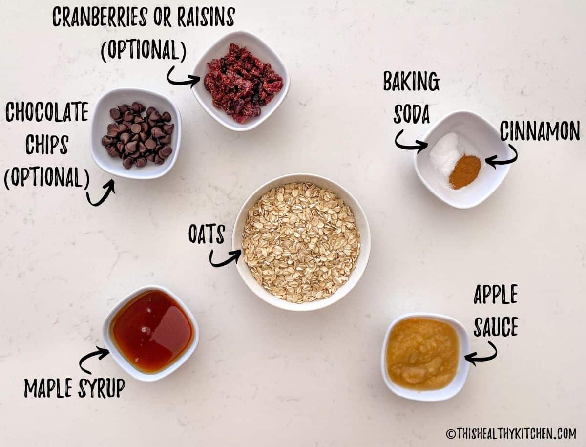 Bowls of rolled oats, applesauce, maple syrup, cinnamon, baking soda, cranberries and chocolate chips.