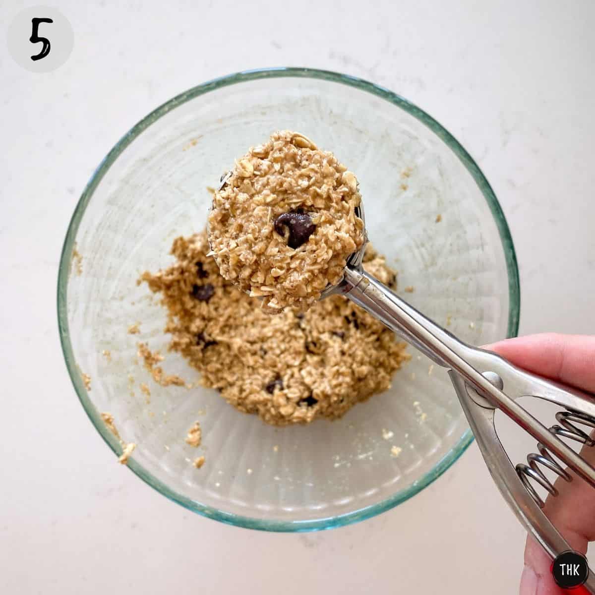 Cookie scoop scooping up cookie batter from large bowl.