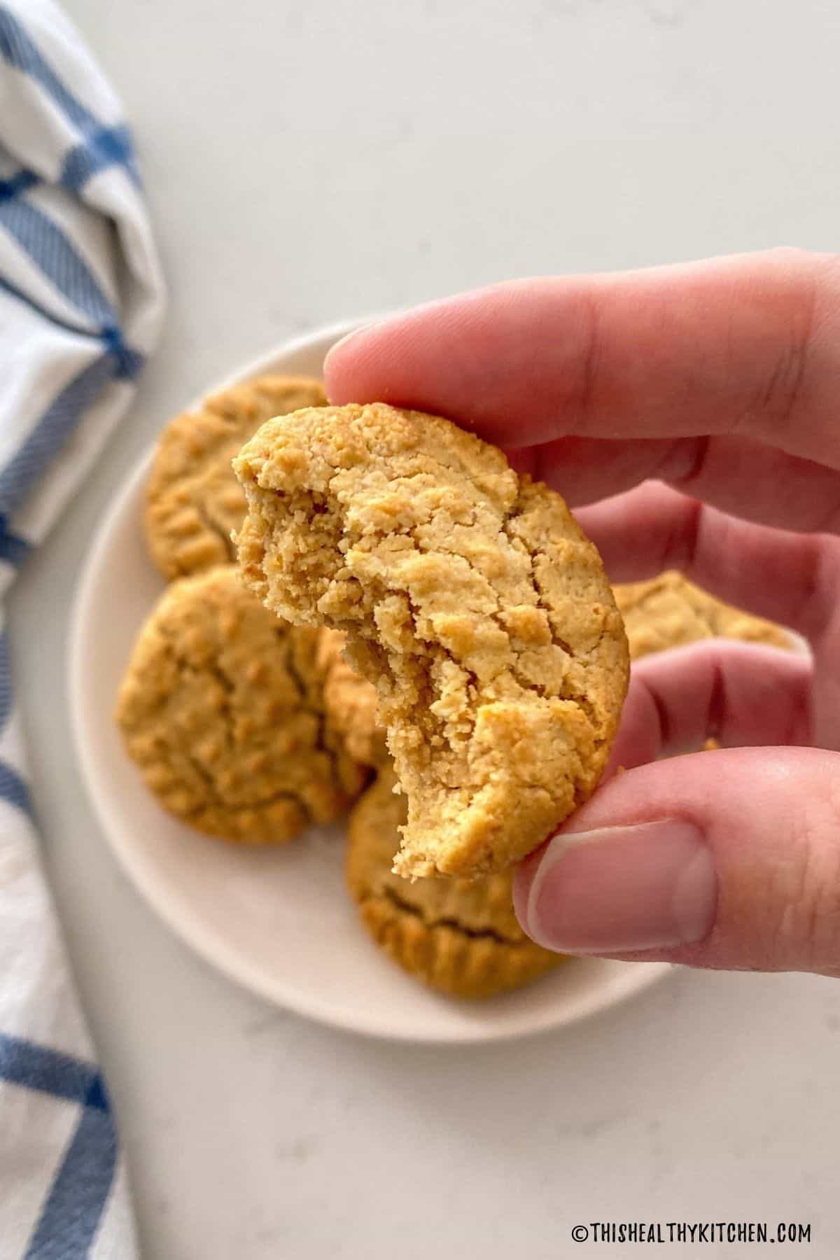 Hand holding up cookie that has been bitted with plate of cookies below.