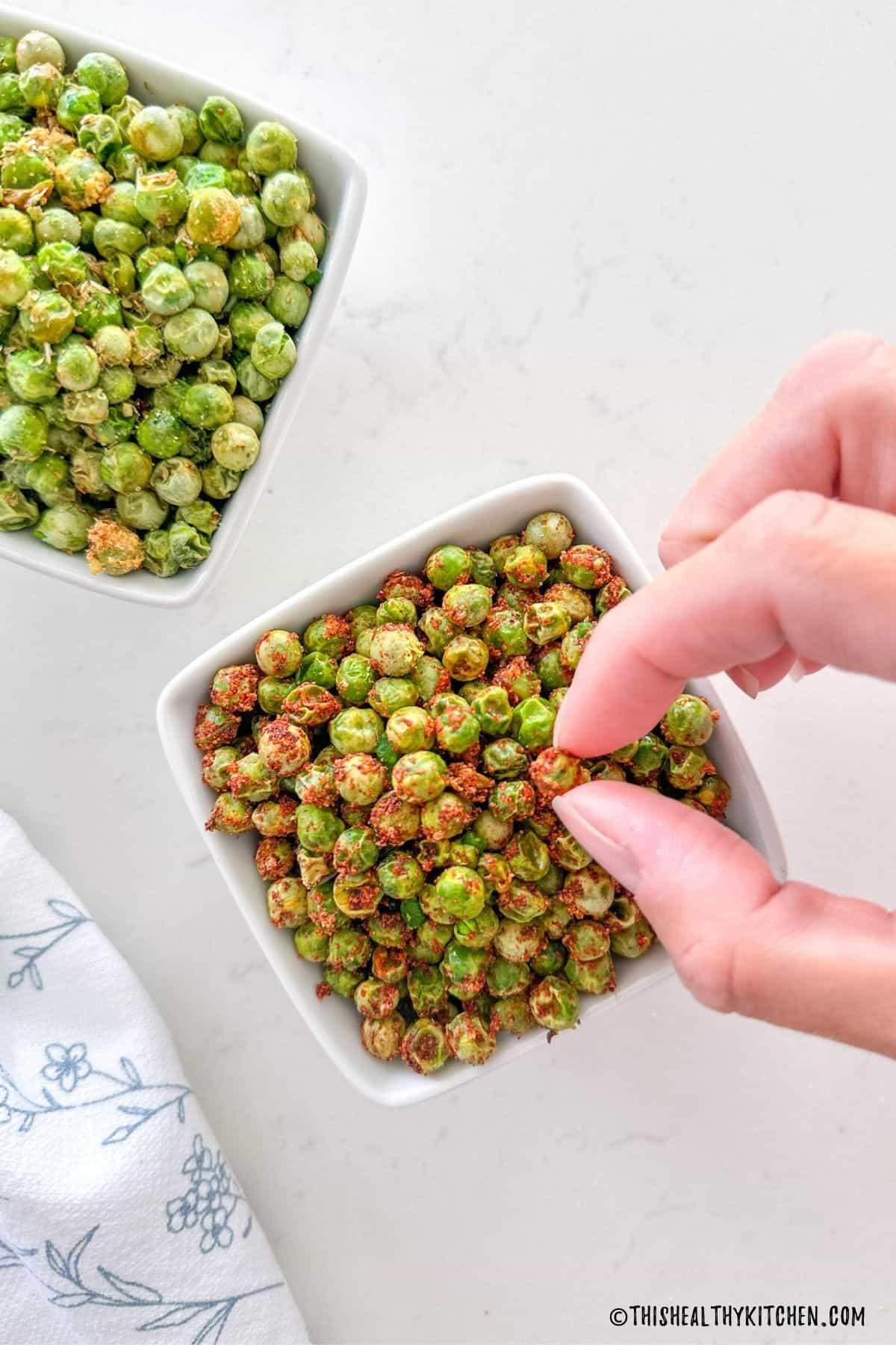 Fingers picking up a pea from bowl of peas.