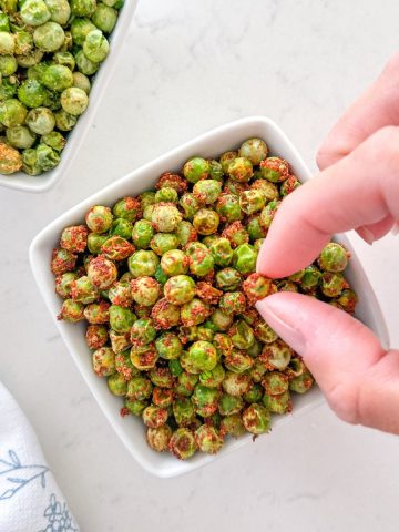 Fingers picking up a pea from bowl of peas.