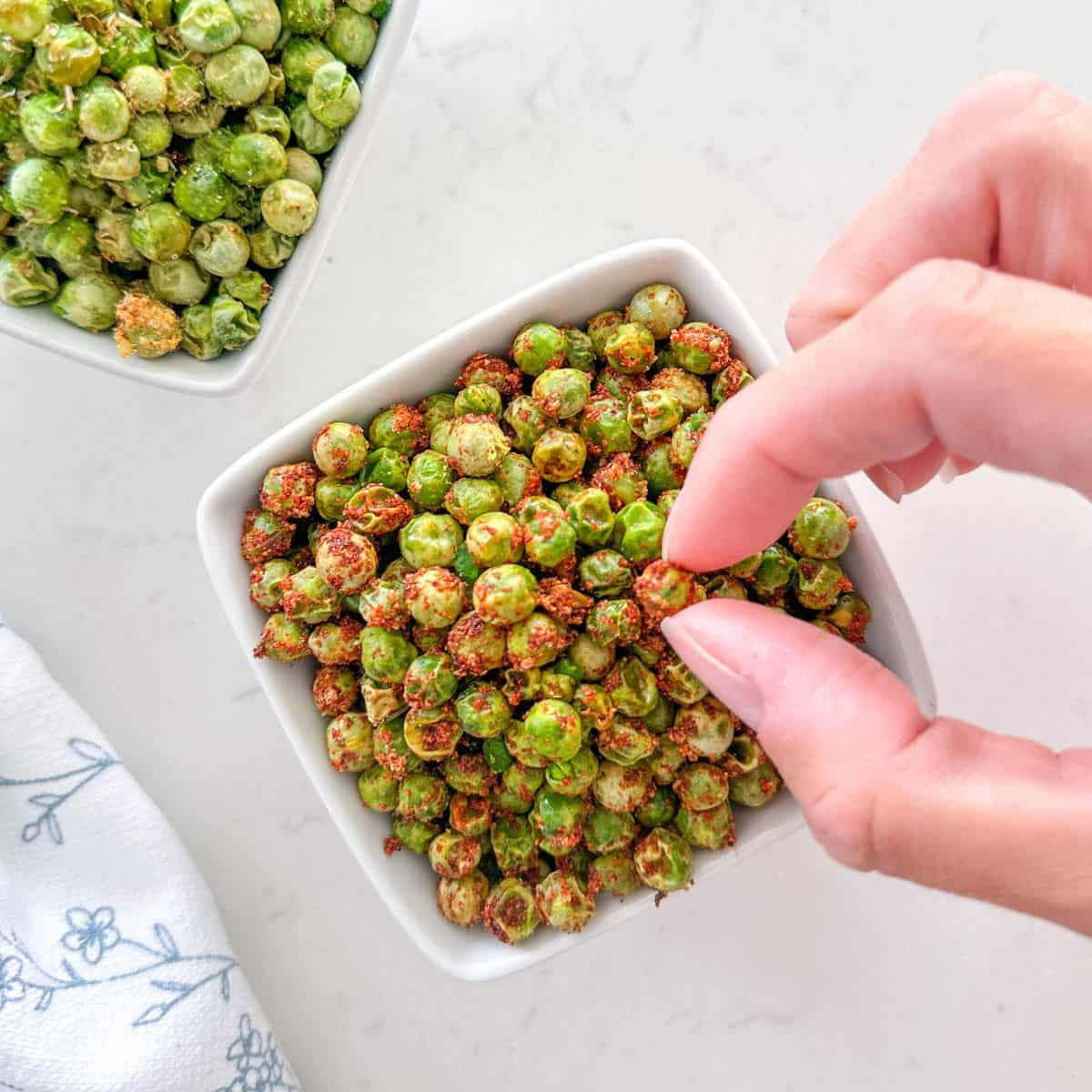 Fingers picking up a pea from bowl of peas.