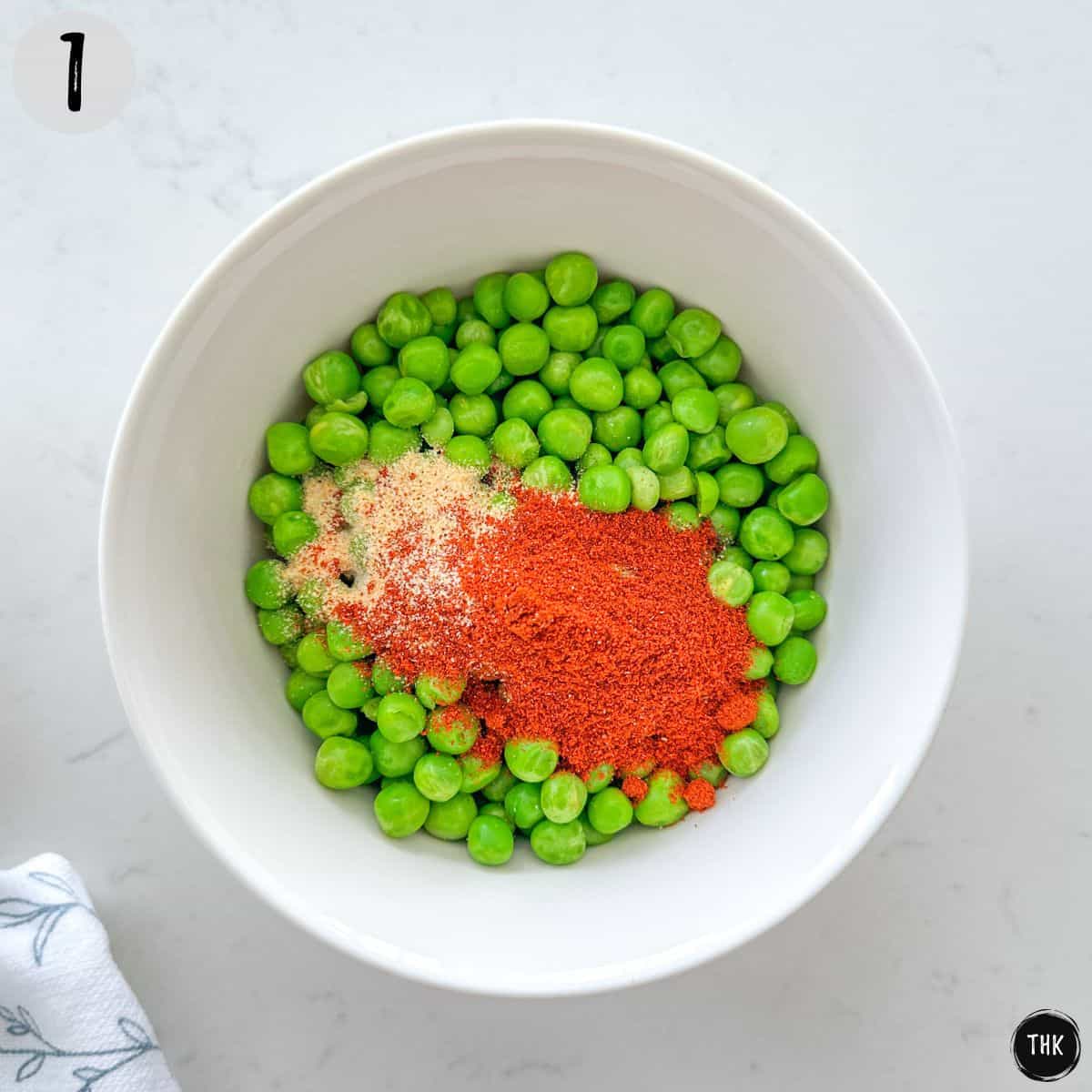 Bowl of green peas with seasoning on top.