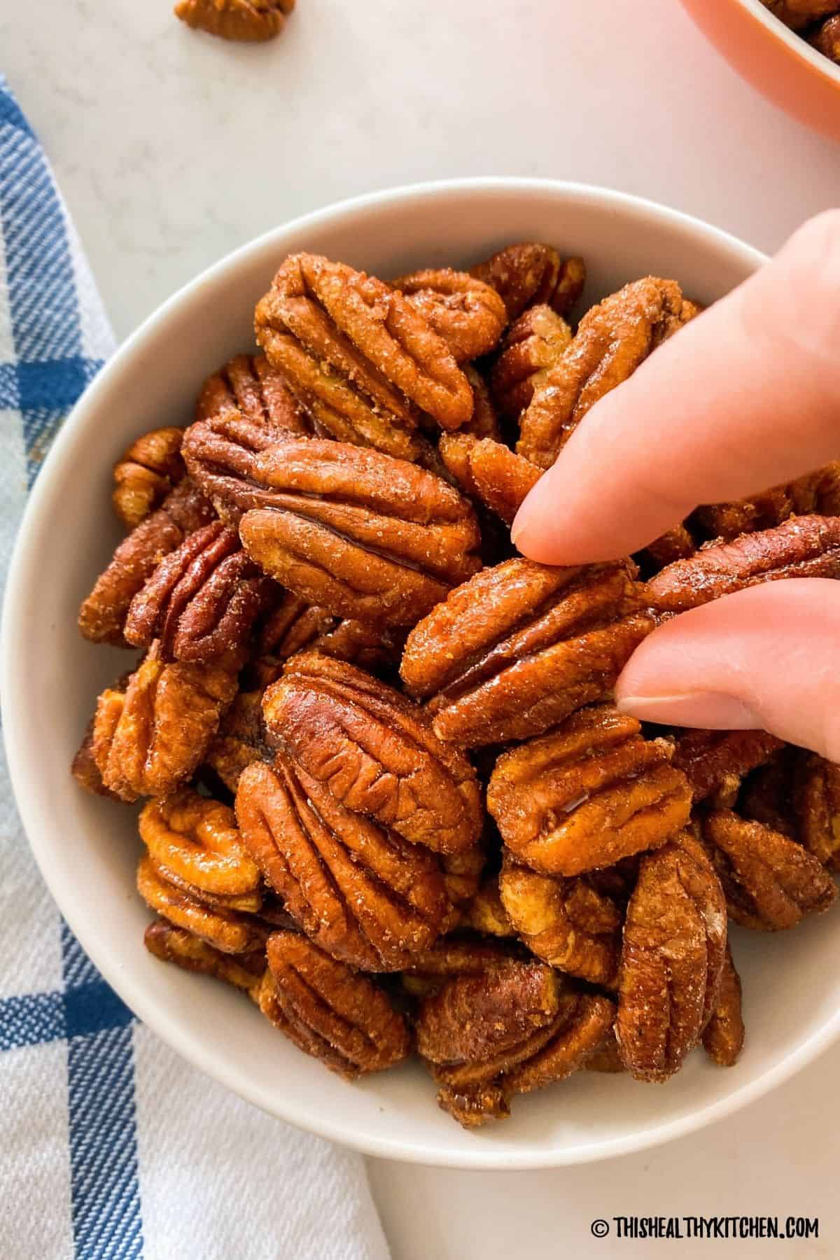 Hand grabbing a pecan half from bowl of pecans.