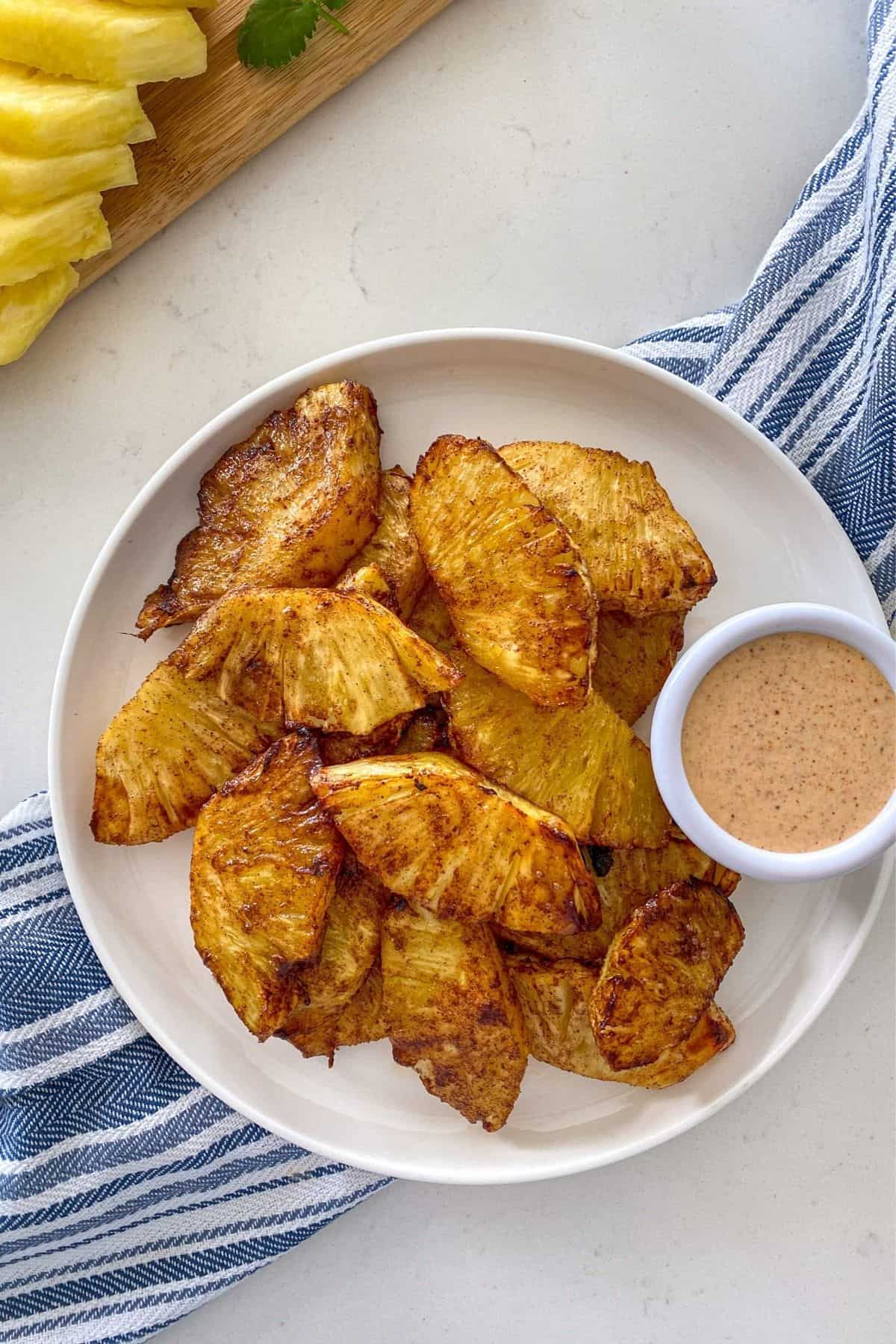 Caramelized pineapple slices in white plate with small bowl of pink dip beside it.