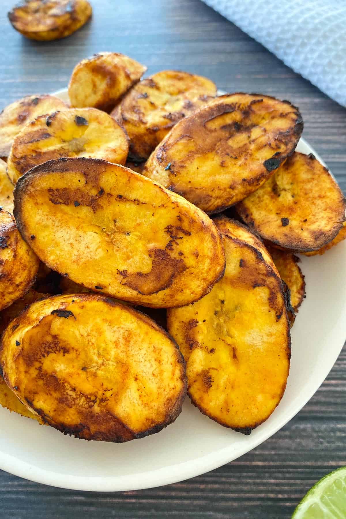 Plantain slices that have been air fried piled onto small white plate.