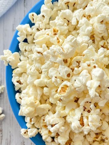 Blue bowl overfilled with popcorn that's spilling over the sides.