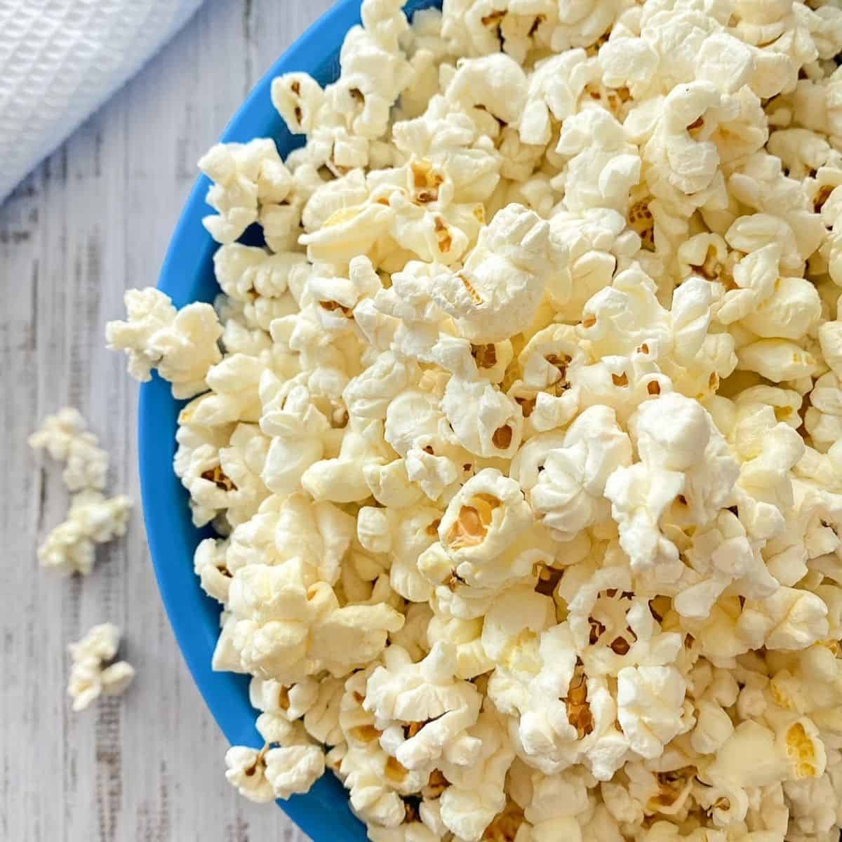 Blue bowl overfilled with popcorn that's spilling over the sides.