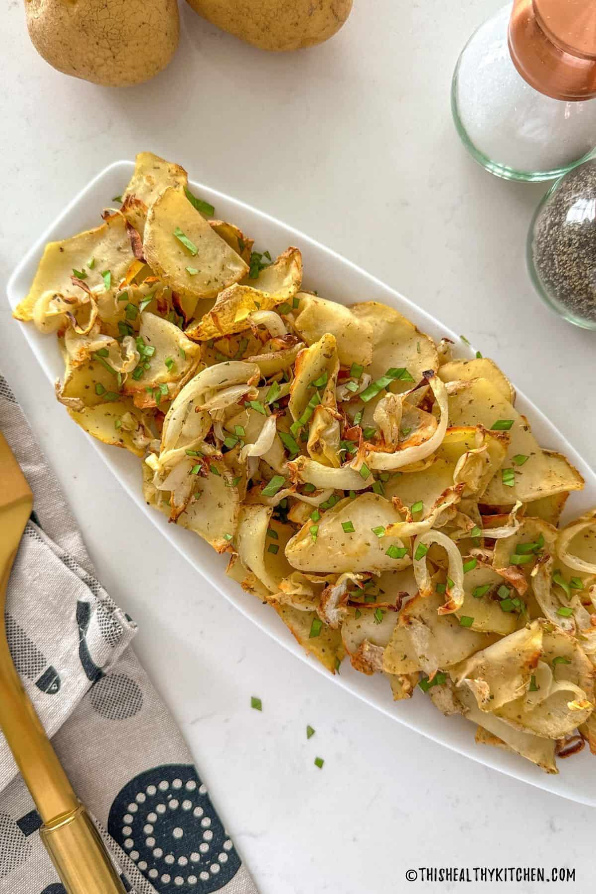 Air fried onions and potatoes in white serving dish with parsley on top.