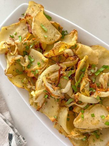 Air fried onions and potatoes in white serving dish.