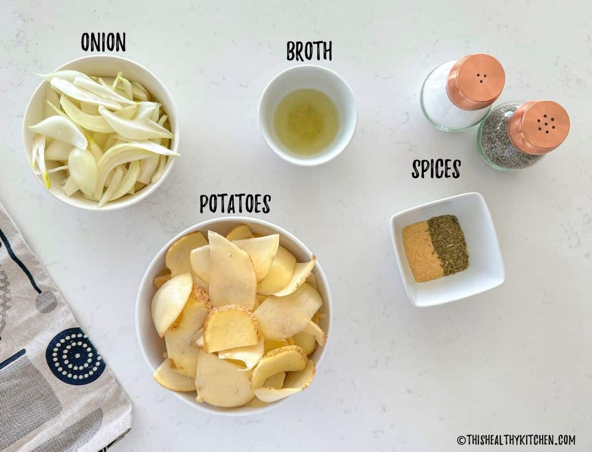 Bowls of sliced potatoes, sliced onions, spices and broth on countertop.