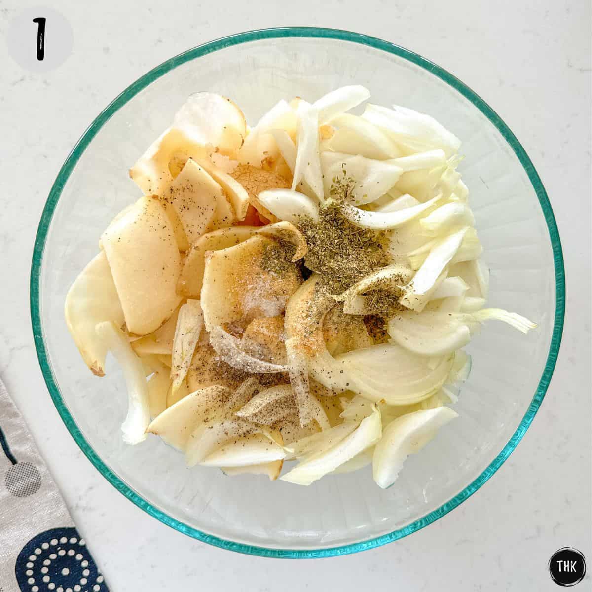 Mixing bowl with sliced potatoes and onions with spices on top.