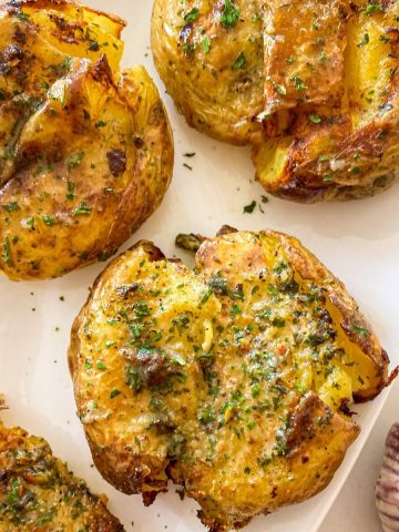 Smashed potatoes on white serving dish with parsley sprinkled on top.
