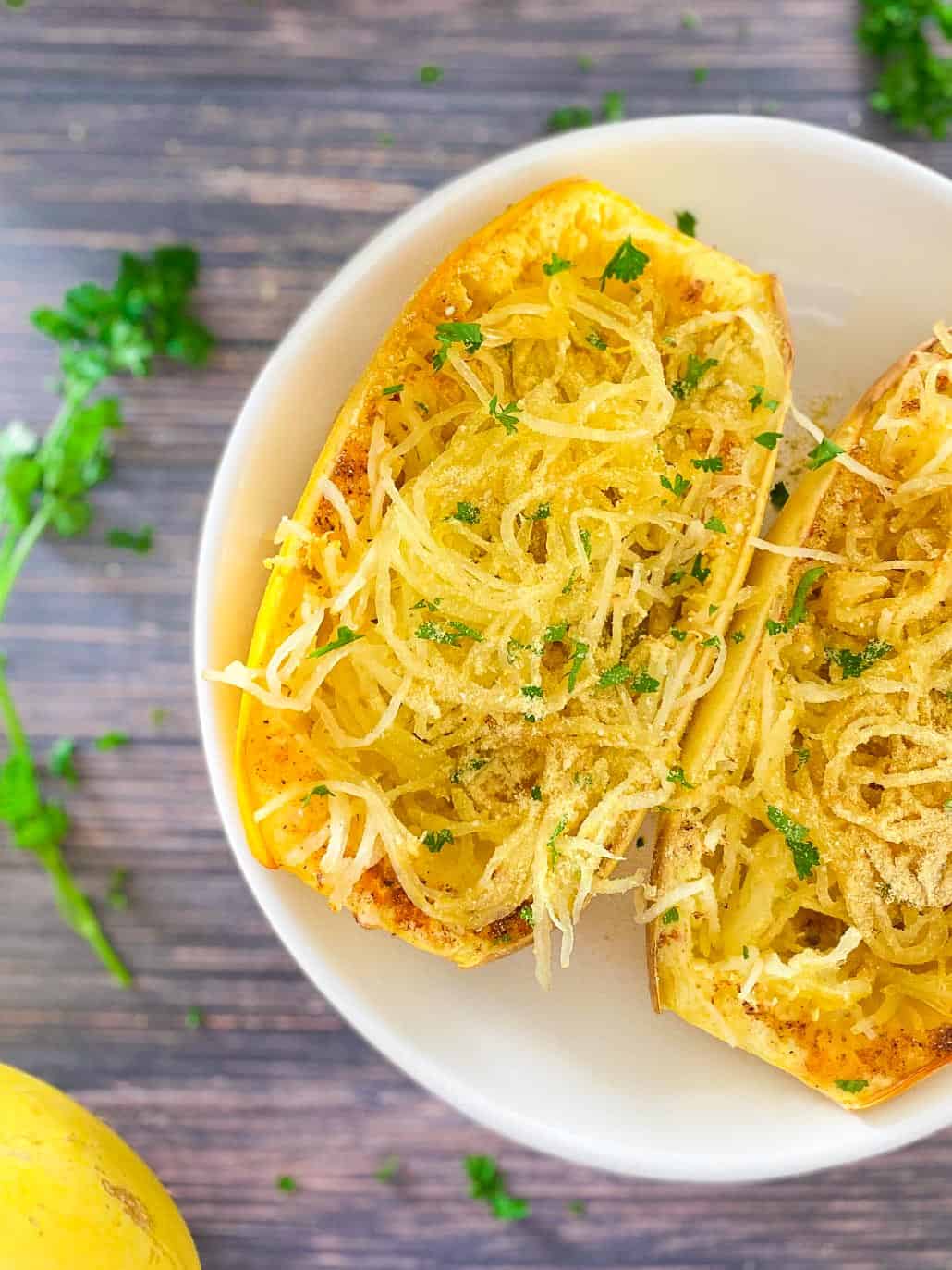 close up of cooked spaghetti squash sliced in half with parmesan cheese and parsley garnish on top.