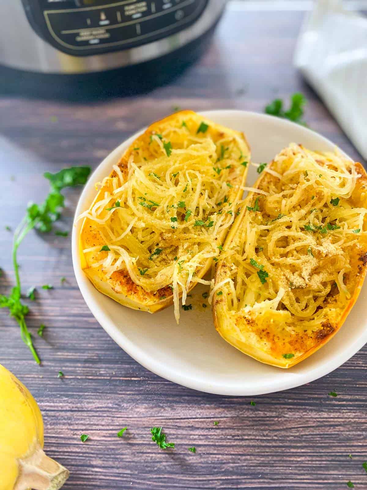 Two halves of a cooked spaghetti squash in white dish with parsley garnish.