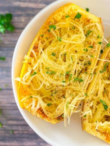close up of cooked spaghetti squash sliced in half with parmesan cheese and parsley garnish on top.
