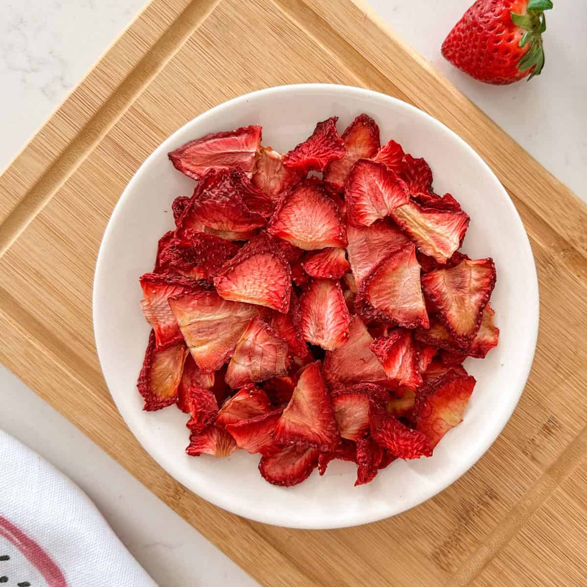 Air fryer strawberries in white plate sitting on cutting board.
