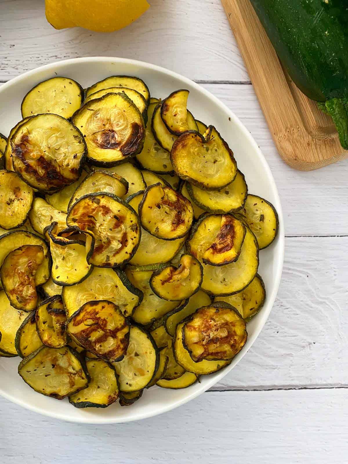 Air fried zucchini in white plate with raw zucchini in background.