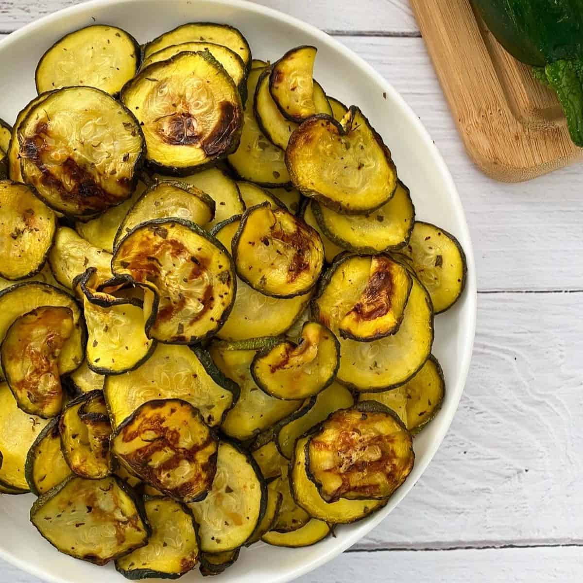 Air fried zucchini in white plate with raw zucchini in background.