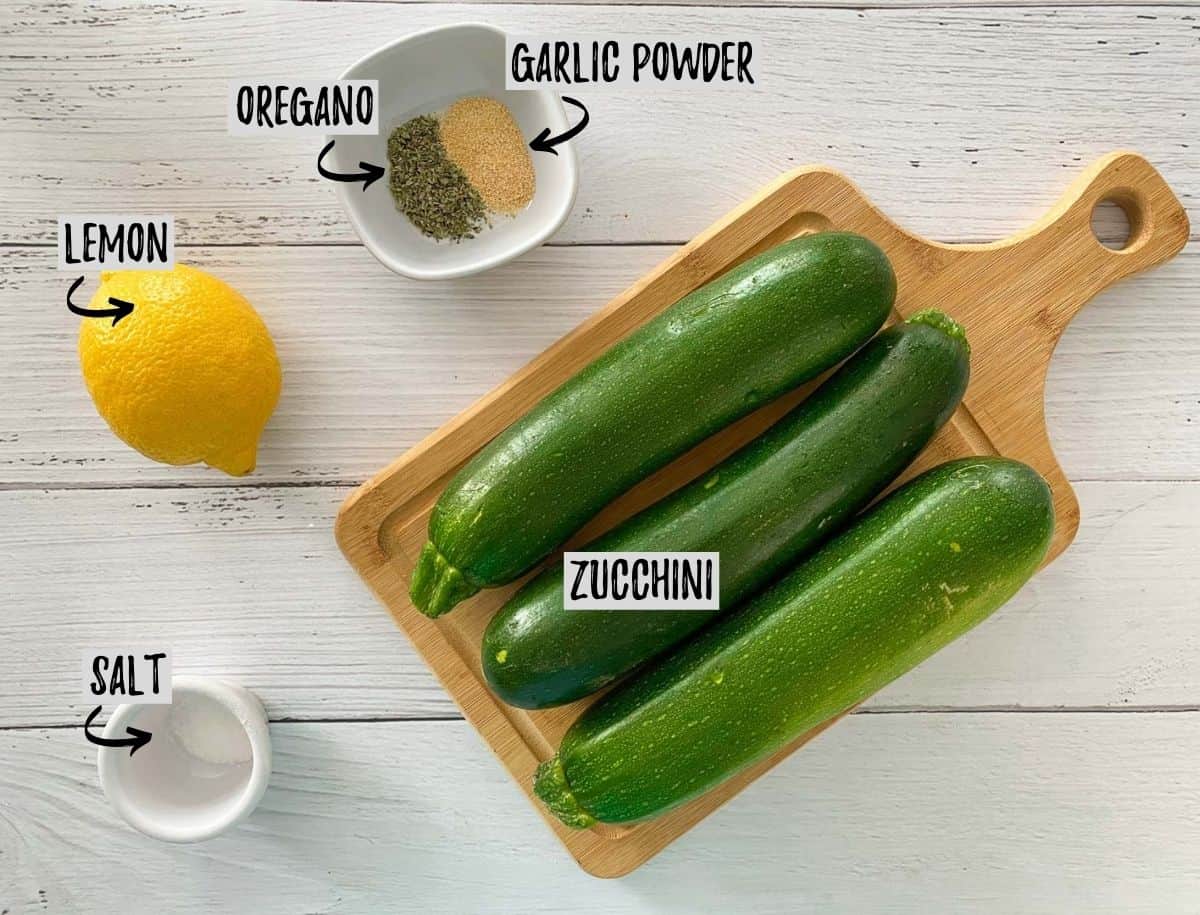 Zucchini on cutting board with lemon and seasoning around it.